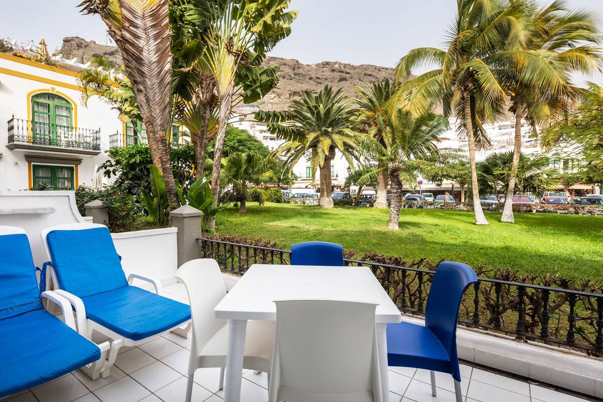 A terrace with white and blue furniture, palm trees, and a view of a mountain.