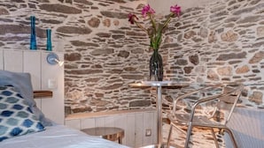 A room with a stone wall, a bed with a blue blanket, a small round table, and a chair.