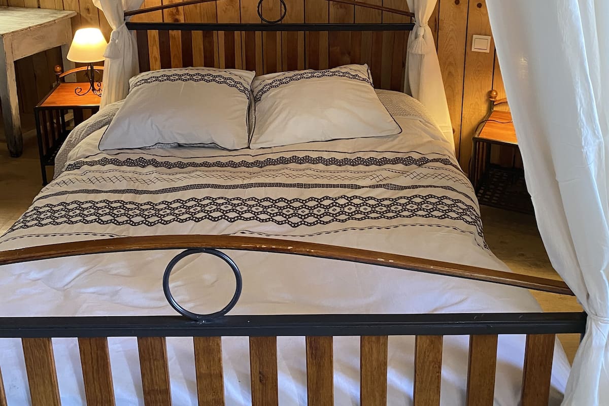 Un lit avec une tête de lit en bois, une literie blanche et un mur en pierre en arrière-plan.