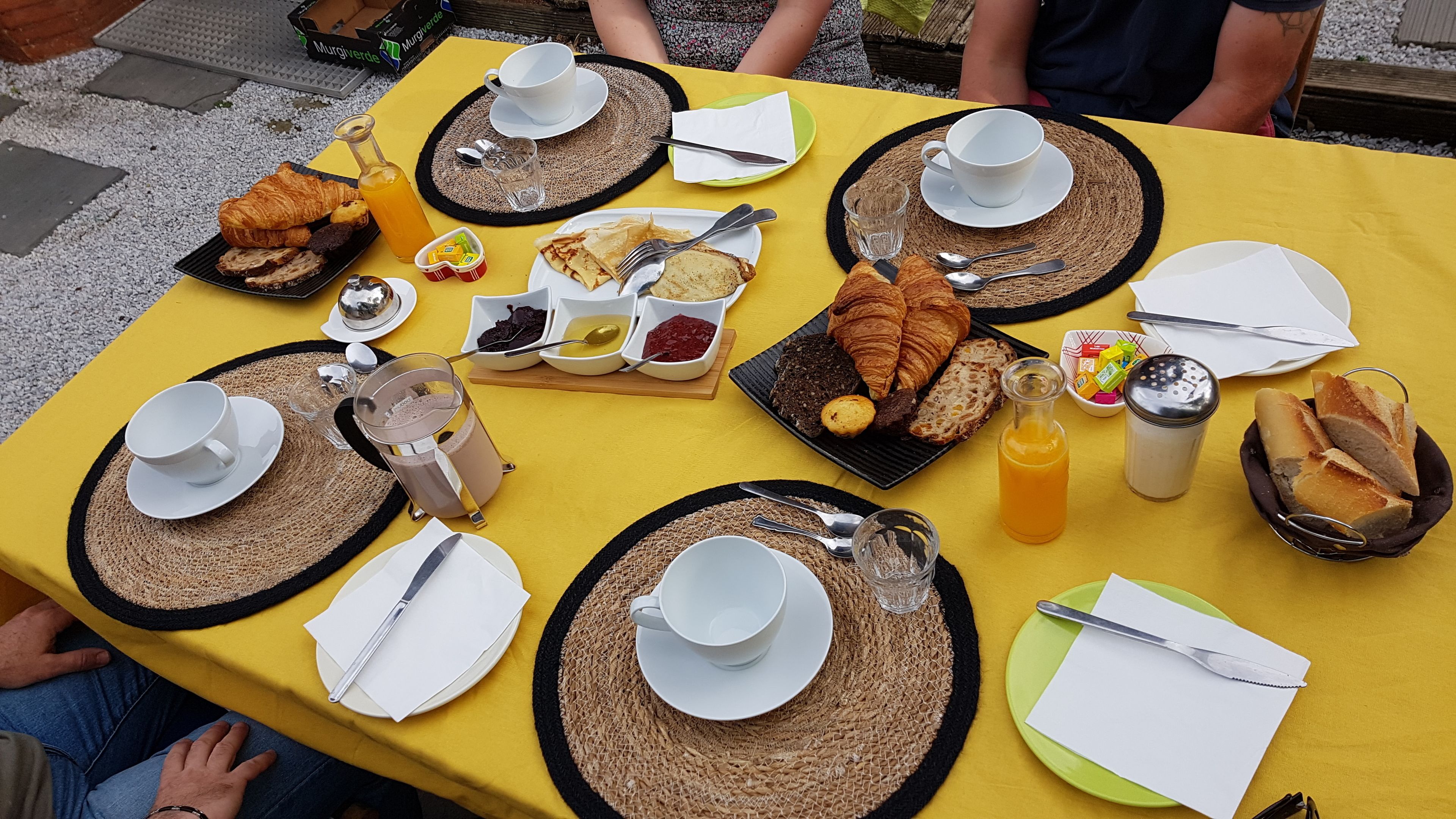 Una mesa lista para el desayuno con croissants, pan y diferentes mermeladas y untables.