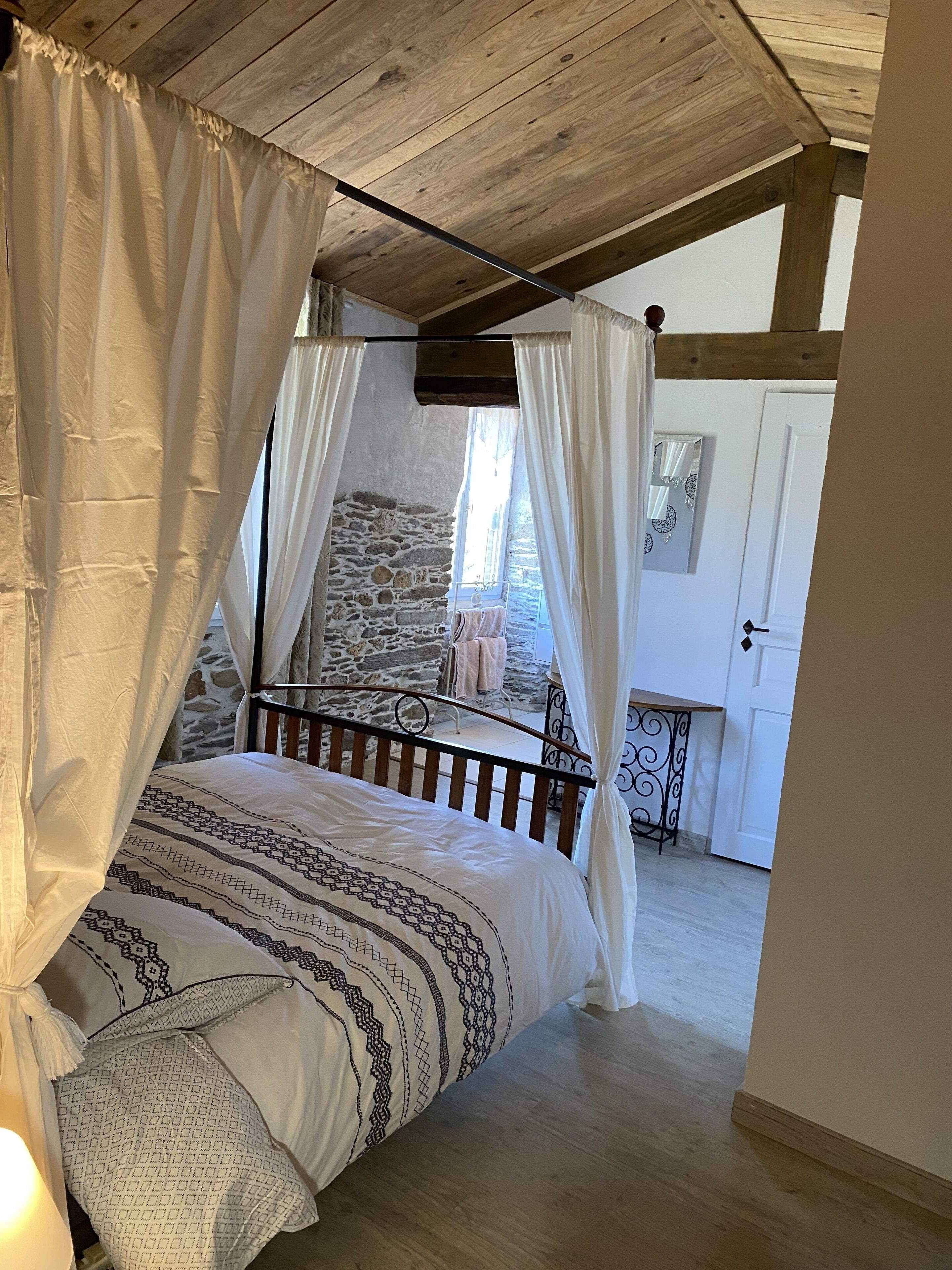 A bedroom with a wooden ceiling, a stone wall, and a balcony with a metal railing.