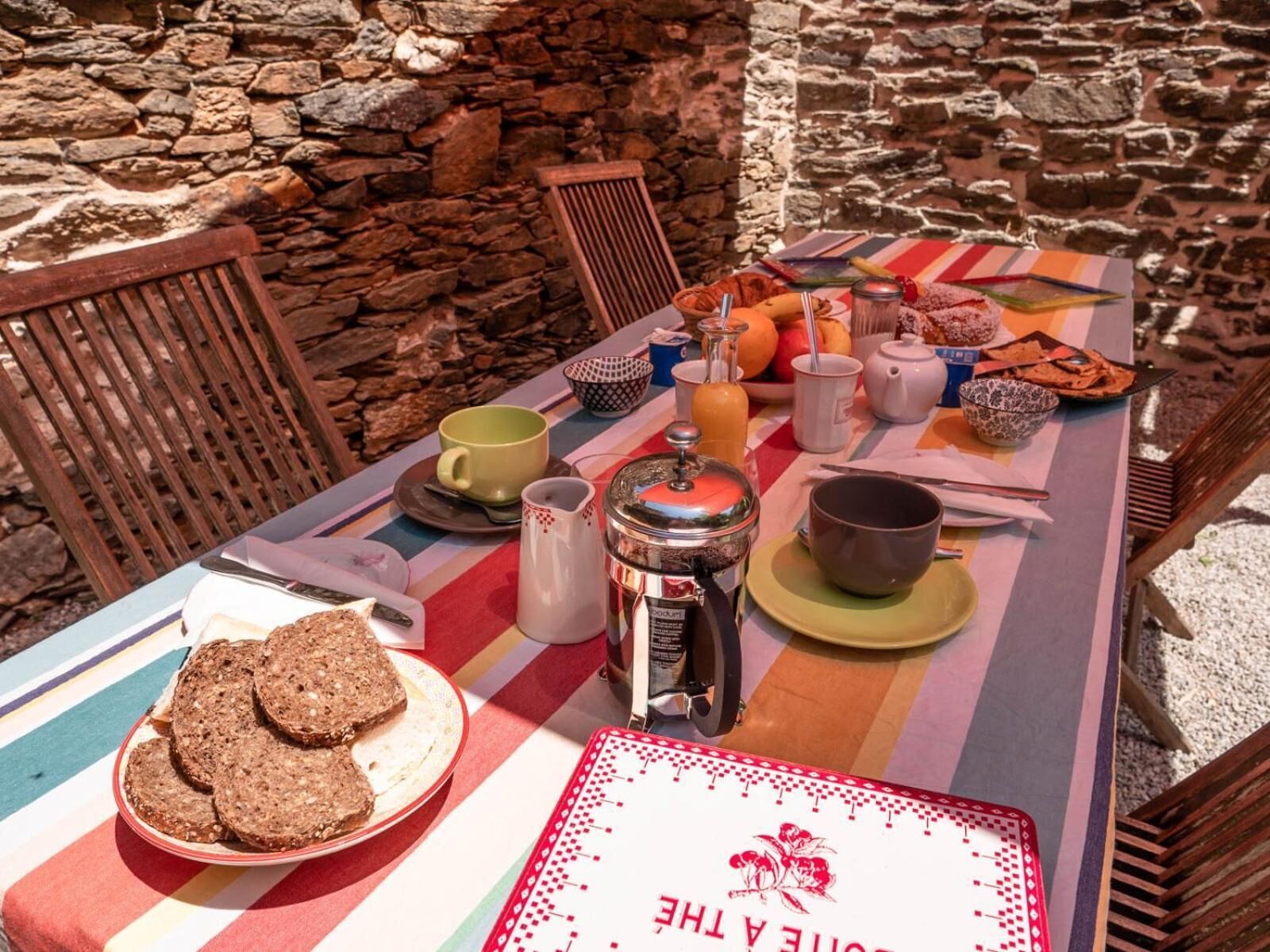 A breakfast table set with bread, fruits, and a coffee pot.