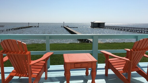 A deck with two wooden chairs and a small table, overlooking a body of water with a pier and a dock.