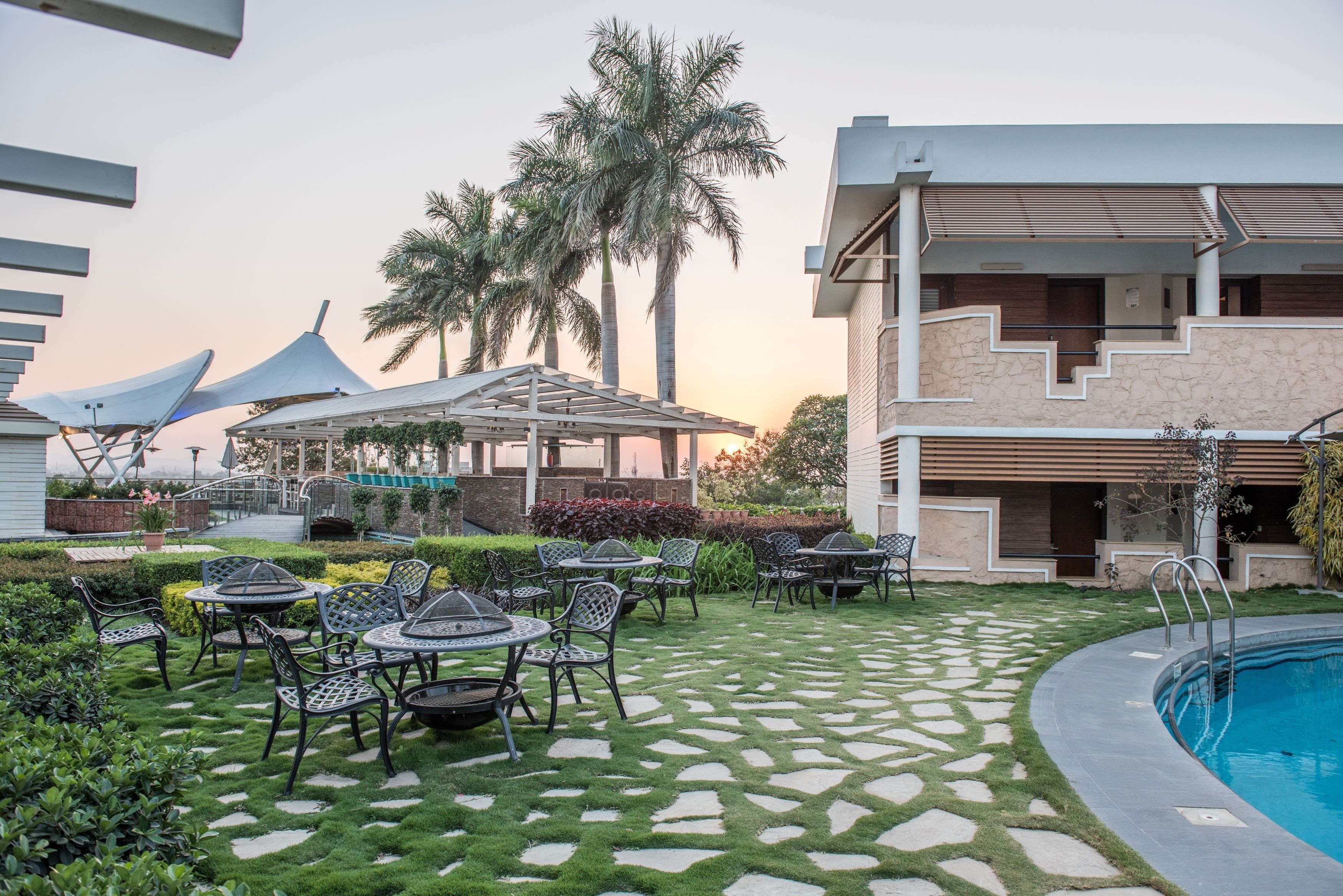 An outdoor patio with a pool, surrounded by palm trees and a modern building.