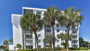 A multi-story hotel with balconies, surrounded by palm trees and well-maintained gardens.