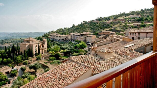 A panoramic view of a hillside town with terracotta-roofed buildings, a prominent church, and lush greenery.