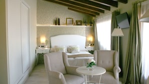 A bedroom with a bed, two armchairs, a small table, a nightstand, and a TV on the wall.
