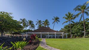 A building with a covered patio area, surrounded by palm trees and a well-maintained lawn. - 2BR Mauna Lani Point with stunning Ocean Views! (Kamuela)