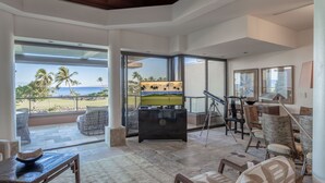 A spacious living area with a large TV, comfortable seating, and a view of the beach. - 2BR Mauna Lani Point with stunning Ocean Views! (Kamuela)