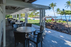 An outdoor patio with tables and chairs, overlooking a beach and ocean.