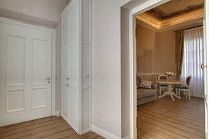 A room with a wooden floor, white walls, and a white door. There is a dining area with a table and chairs, and a sofa.