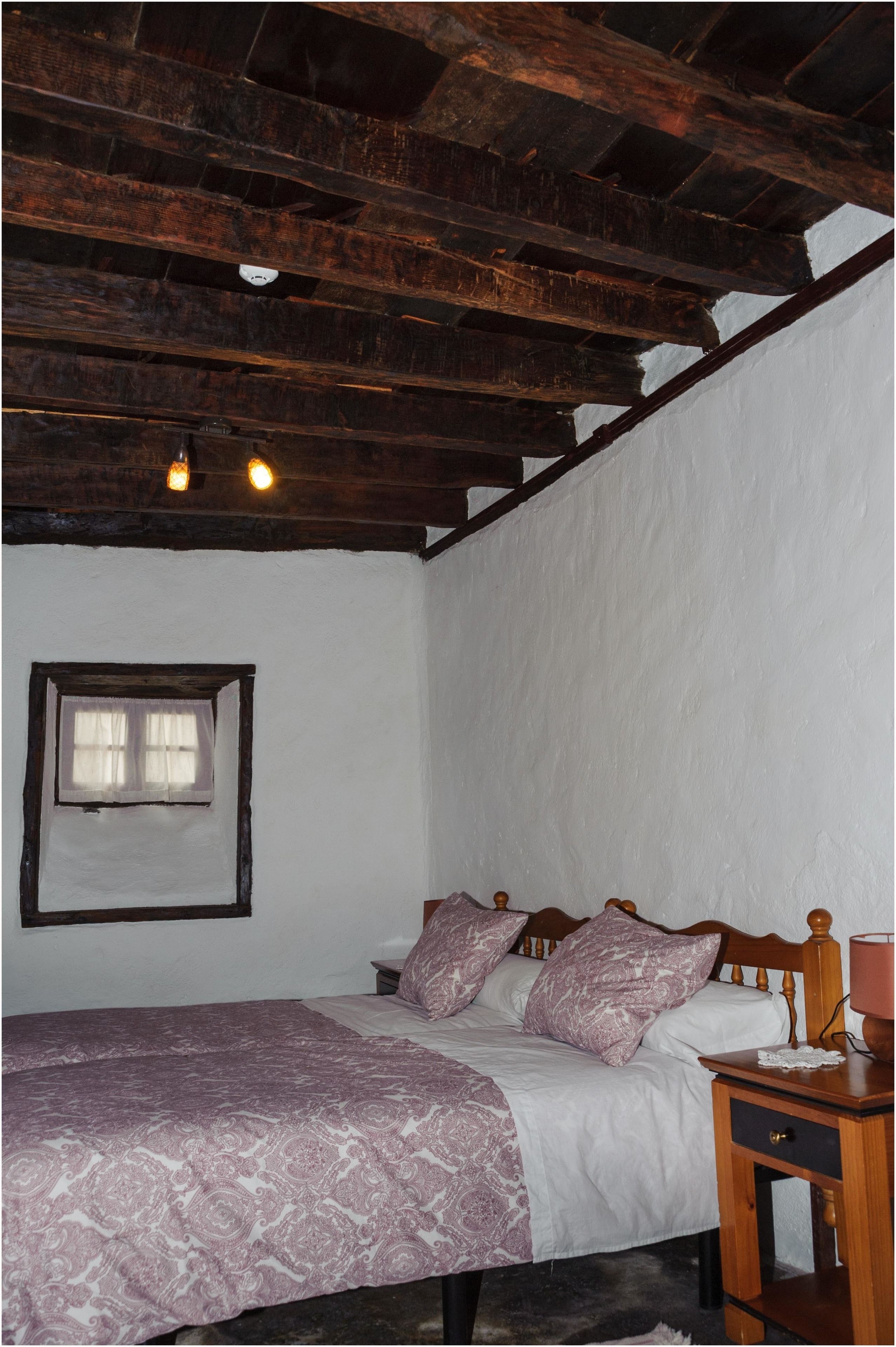 A bedroom with a wooden bed, a nightstand, a window with curtains, and a white wall.