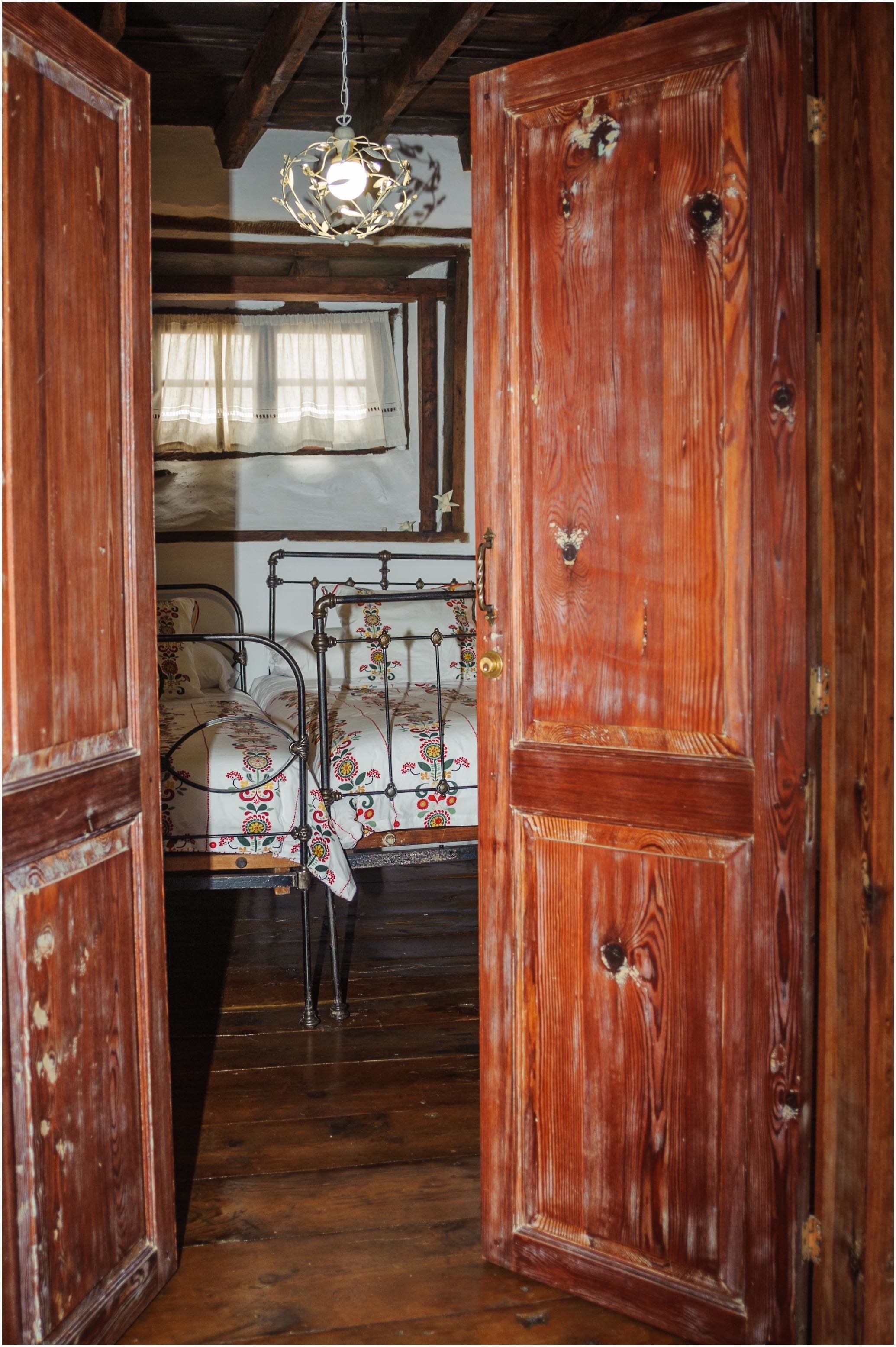 Una puerta de madera con manija de latón, una cama con colcha de motivos florales y una lámpara colgante.