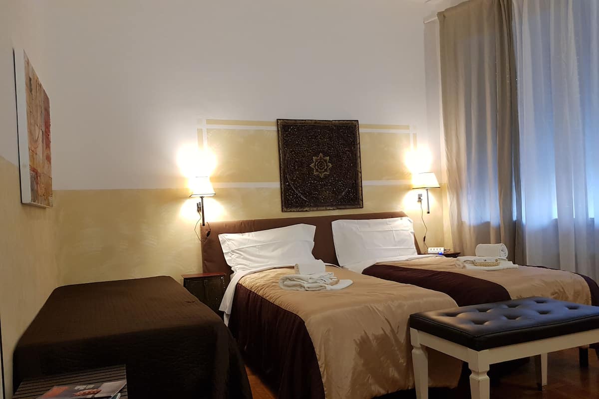 Hotellihuone, jossa on kaksi sänkyä, penkki ja pöytä.