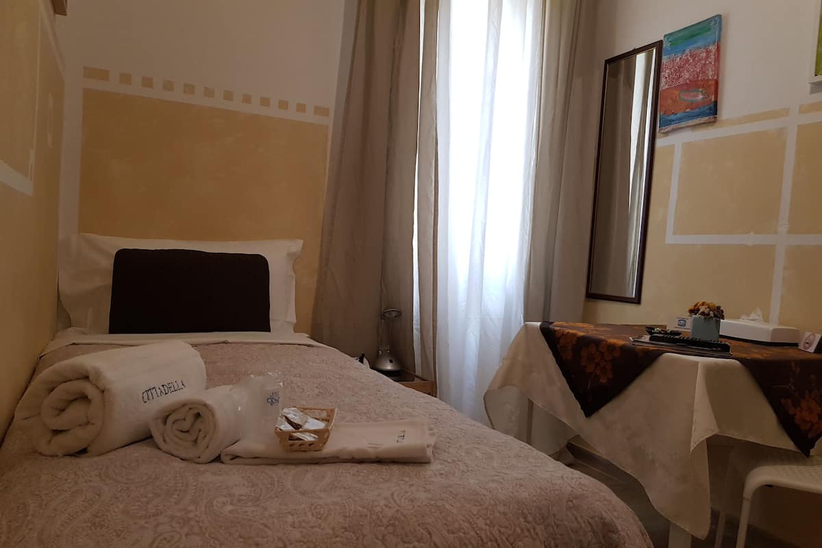 Hotellihuone, jossa on sänky, pöytä maljakolla ja peili seinällä.