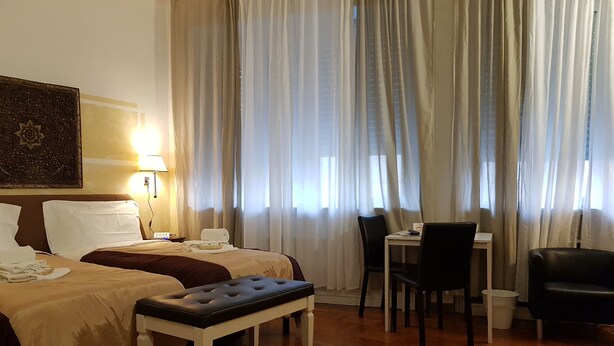 A hotel room with two beds, a dining table, chairs, a bench, and a painting on the wall. - Locazione Turistica Cittadella (Verona)