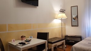 A hotel room with a bed, a desk with a chair, a television mounted on the wall, a lamp, a mirror, and a small table with a chair. - Locazione Turistica Cittadella (Verona)