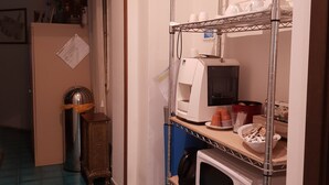 A kitchen area with a microwave, toaster, and shelves holding cups and plates. - Locazione Turistica Cittadella (Verona)