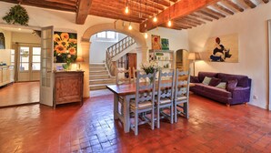 Un vaste espace de vie comprenant une table à manger en bois, des chaises et un canapé violet. Un escalier mène à l’étage supérieur, et un tableau est visible sur le mur.