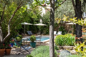 Zona de piscina con sillones de descanso, sombrillas y plantas en macetas.