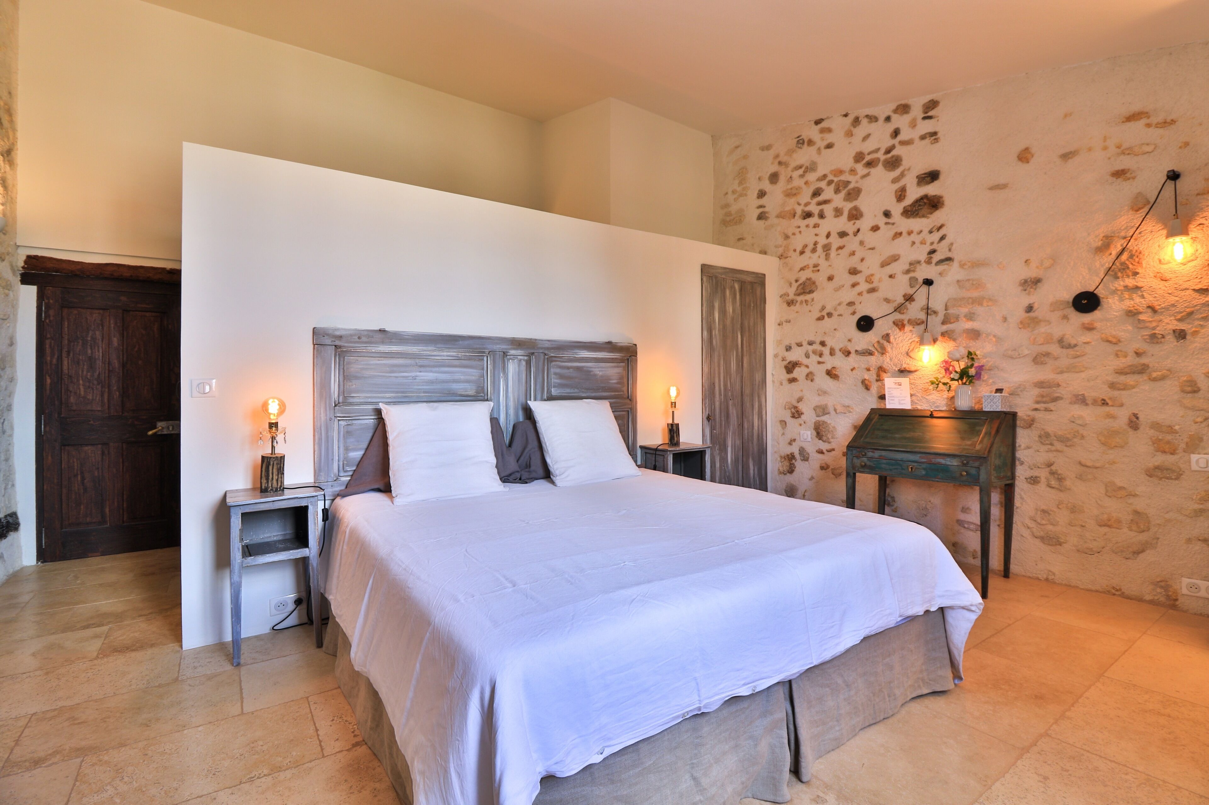 A bedroom with a large bed, a stone wall, and a wooden door.