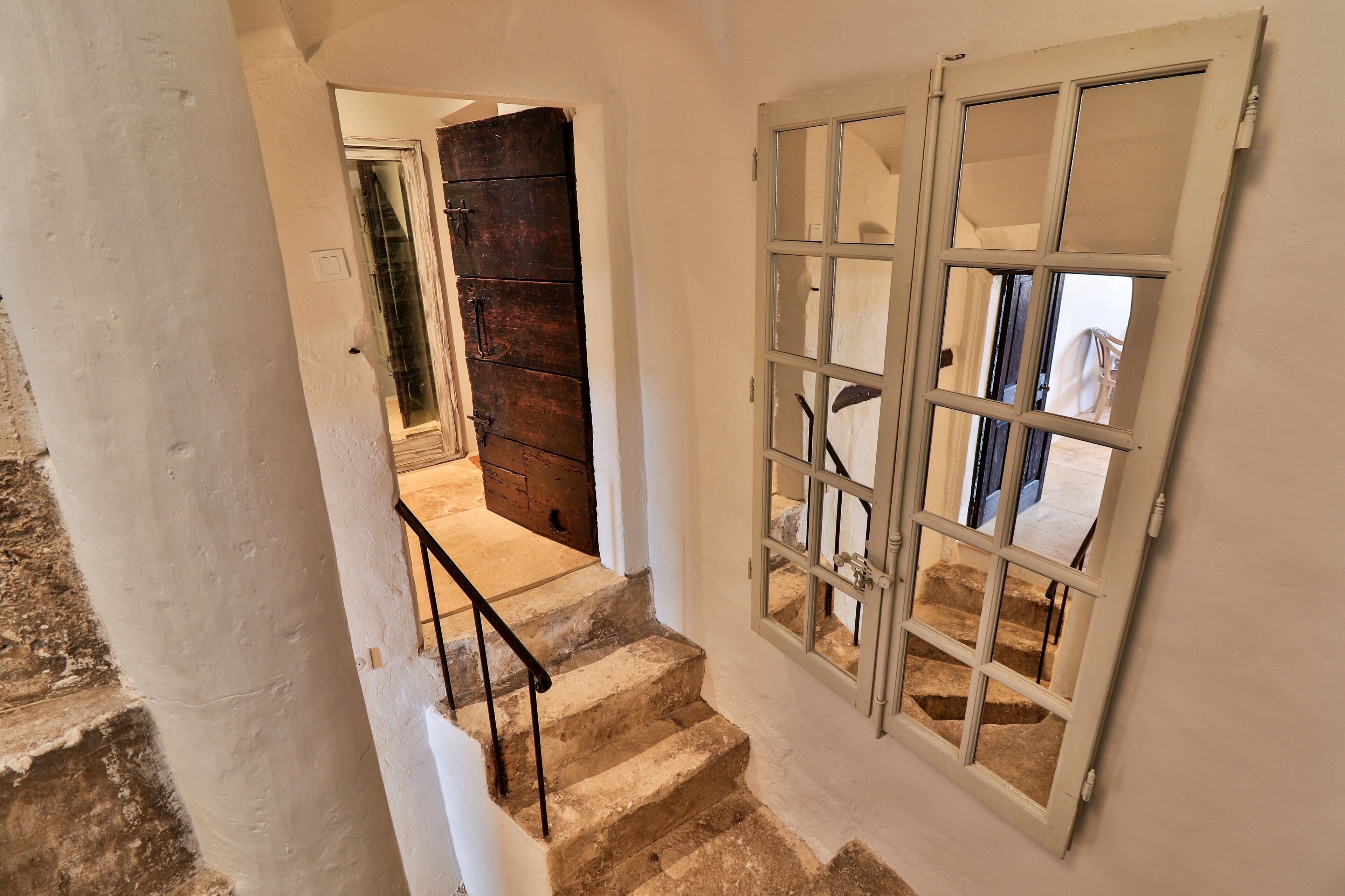 Una escalera de piedra con barandilla de metal que lleva a una habitación con un ventanal y una puerta de madera.