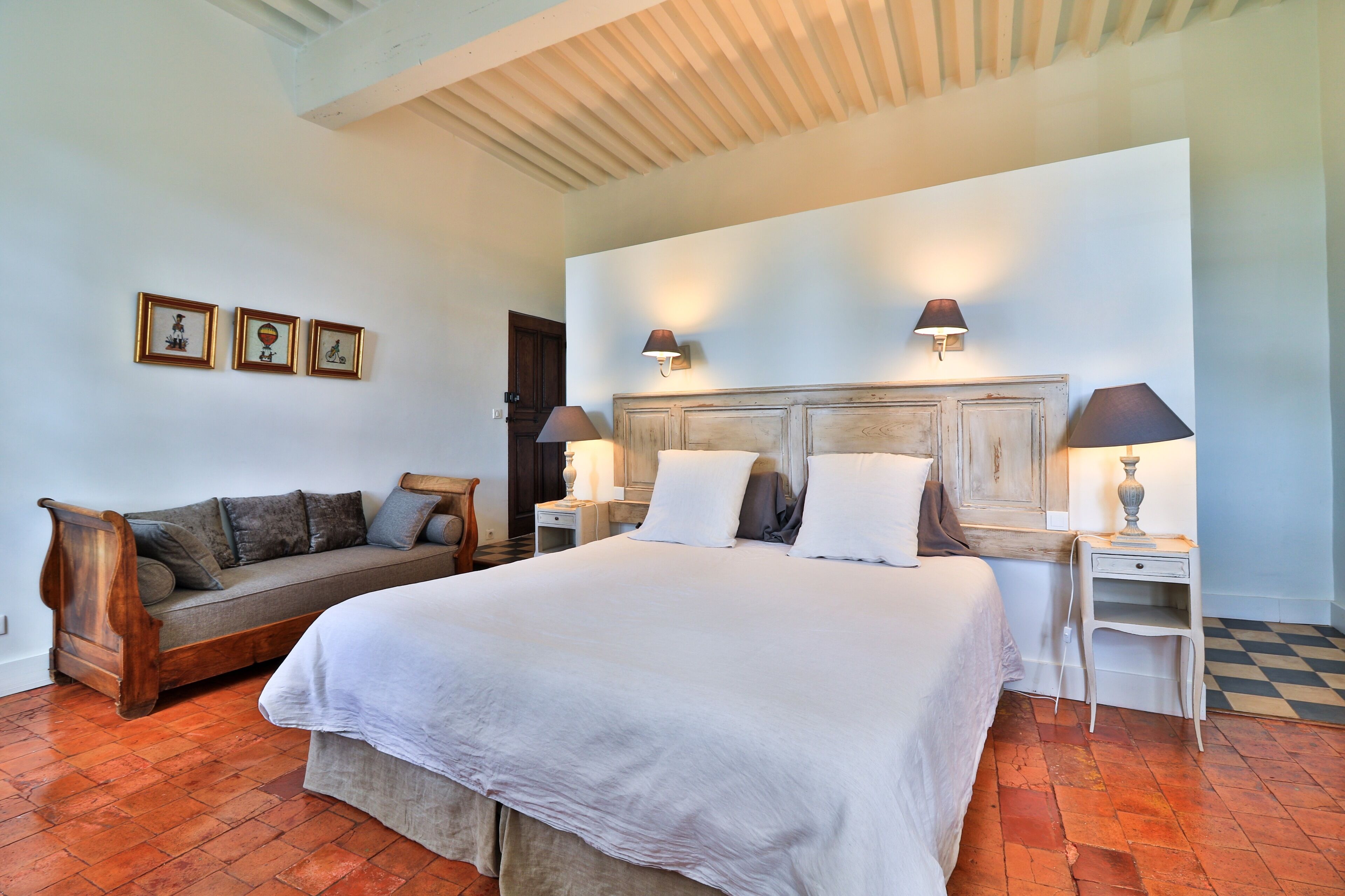 A bedroom with a large bed, a wooden bench, and a small table with lamps.