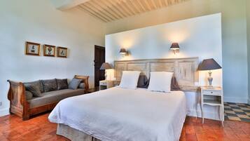A bedroom with a large bed, a wooden bench, and a small table with lamps.