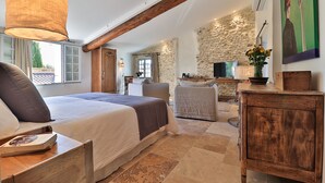 Une chambre à coucher avec un grand lit, une tête de lit en bois, un mur en pierre, une armoire en bois et un tableau accroché au mur.