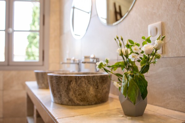 Un baño con lavamanos de mármol, un espejo y un florero con flores.