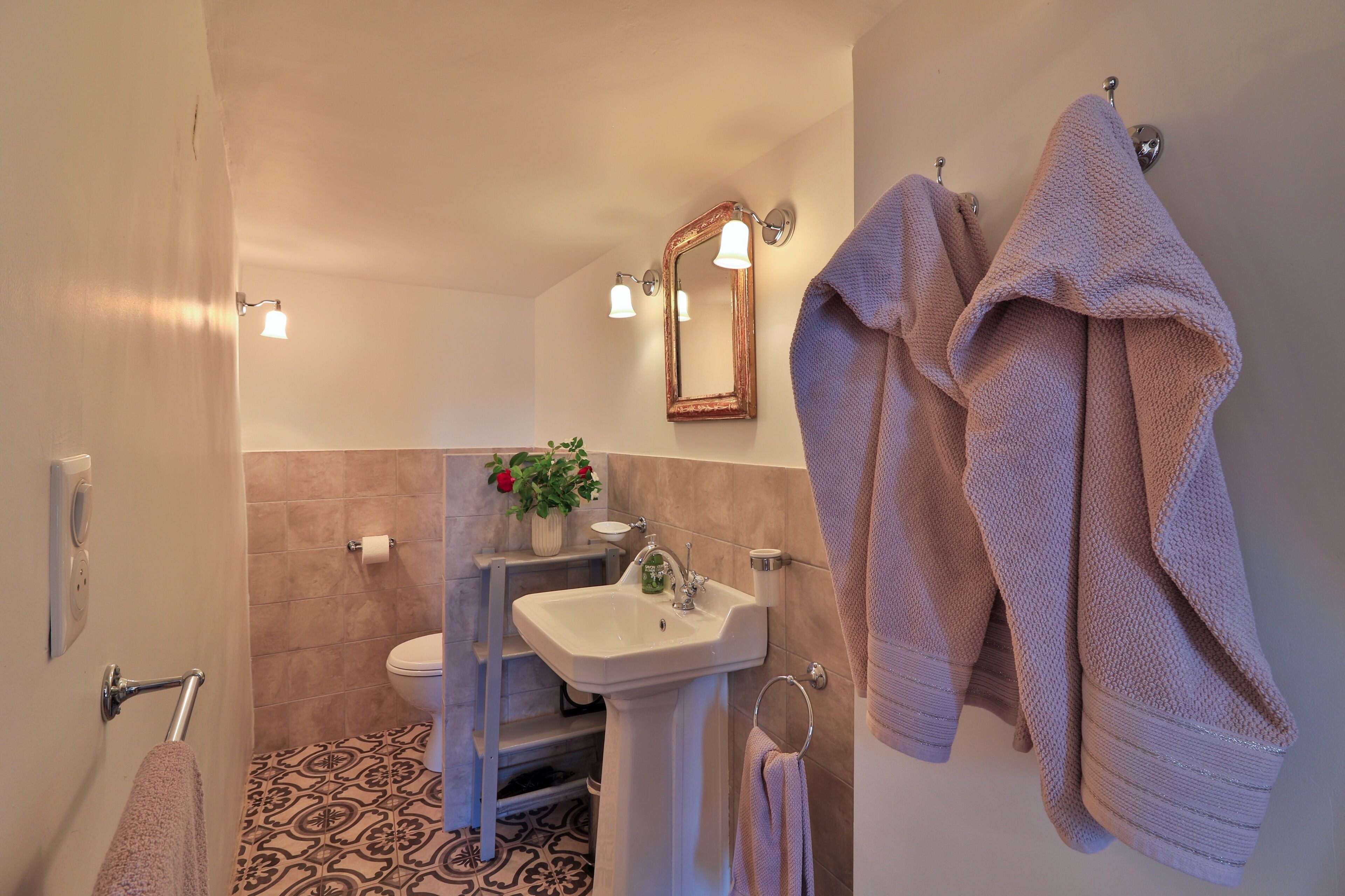 Baño con lavamanos, espejo, toallero y baldosas de suelo con diseño.