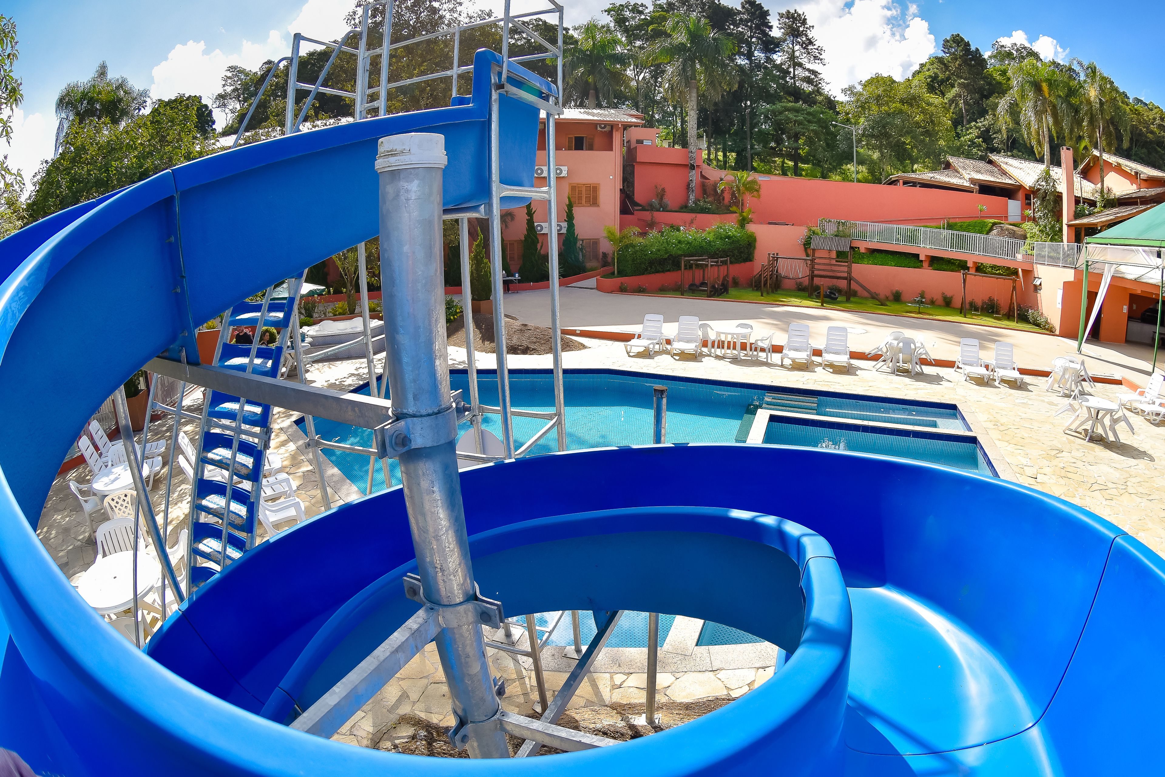 Un tobogán de agua con zona de piscina, sillas de descanso y un edificio de fachada roja.