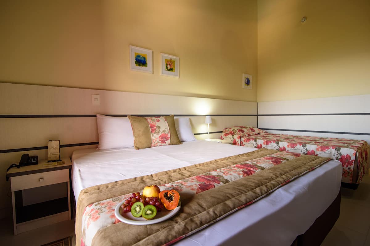 A hotel room with two beds, a bedside table with a phone, and a plate of fruit on the bed.