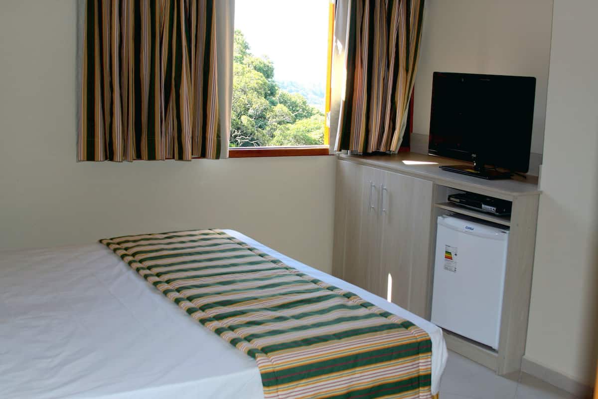 A hotel room with a bed, a television, a mini-fridge, and curtains over a window.