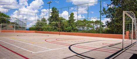 An outdoor basketball court with a goal post, surrounded by trees and a clear sky.