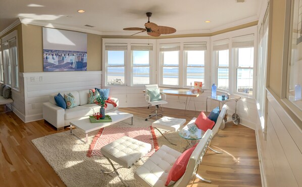 Un salón amplio con un sofá blanco, una mesa de centro y un sillón. Grandes ventanales con vistas a la playa.