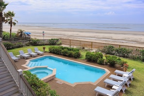 A swimming pool with lounge chairs, a wooden deck, and a view of the beach.