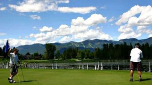 Um campo de golfe com montanhas ao fundo, uma bandeira e uma pessoa em primeiro plano.