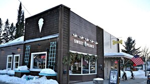 Um edifício com uma placa que diz 'SWEET PEAKS' e uma pequena área externa com mesas, coberta de neve.