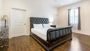A bedroom with a large bed, a dresser, a ceiling fan, and a window with curtains. - 15% OFF Monthly |10% OFF Weekly-Carondelet Street Inviting Condos (New Orleans)