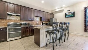 A modern kitchen with dark wood cabinets, stainless steel appliances, a large island with bar stools, and a flat-screen TV mounted on the wall. - 15% OFF Monthly |10% OFF Weekly-Carondelet Street Inviting Condos (New Orleans)