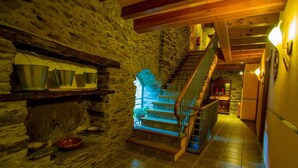 A stone-walled hallway with a wooden staircase, metal buckets on a shelf, and a red bowl on the floor. - Mas D'en Roqueta (Montferrer I Castellbo)