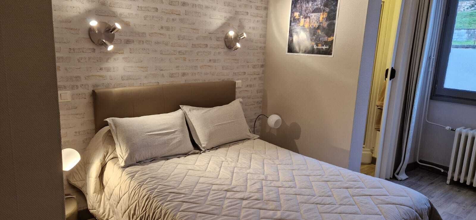 A bedroom with a brick-patterned wall, a bed with two pillows, wall-mounted lights, and a poster.