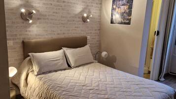 A bedroom with a brick-patterned wall, a bed with two pillows, wall-mounted lights, and a poster.