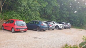 A gravel parking area with several cars parked along a dirt path surrounded by dense green foliage. - Le Faubourg (Figeac)
