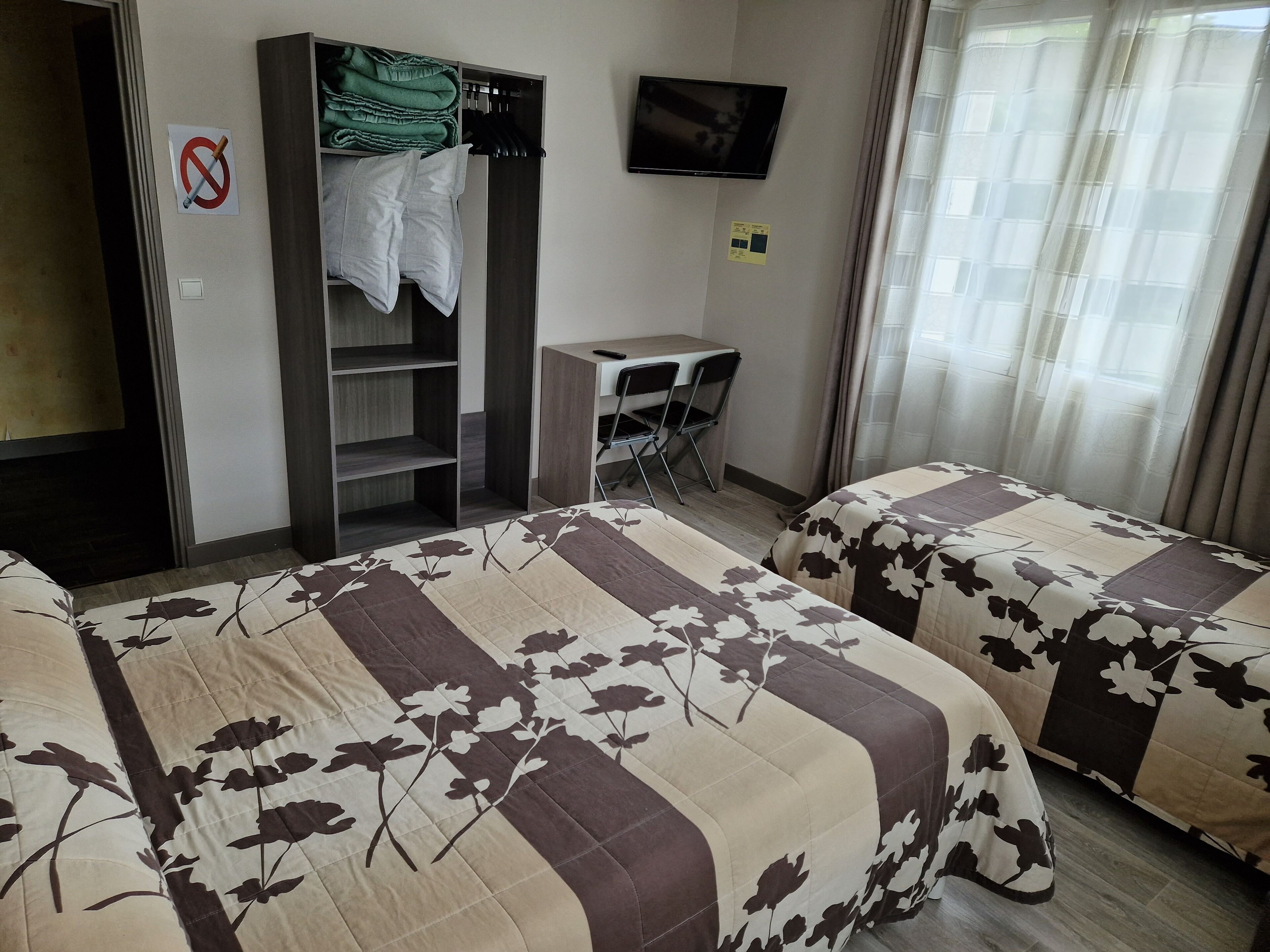 A hotel room with two beds, a desk, a TV, and a wardrobe.
