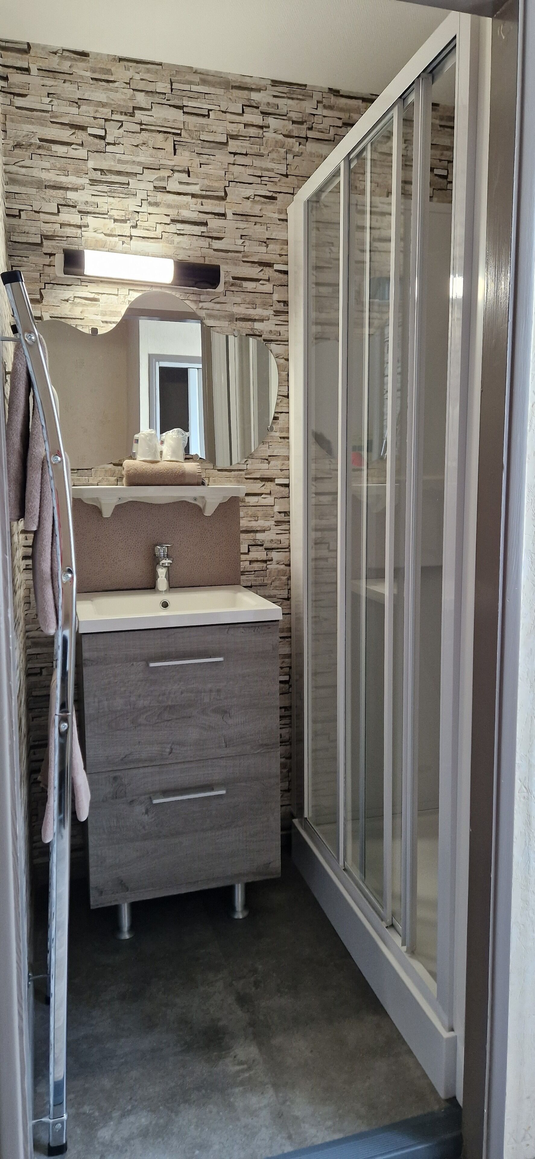 A bathroom with a stone wall, a sink with a mirror above it, and a shower with a glass door.