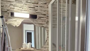 A bathroom with a stone wall, a sink with a mirror above it, and a shower with a glass door.