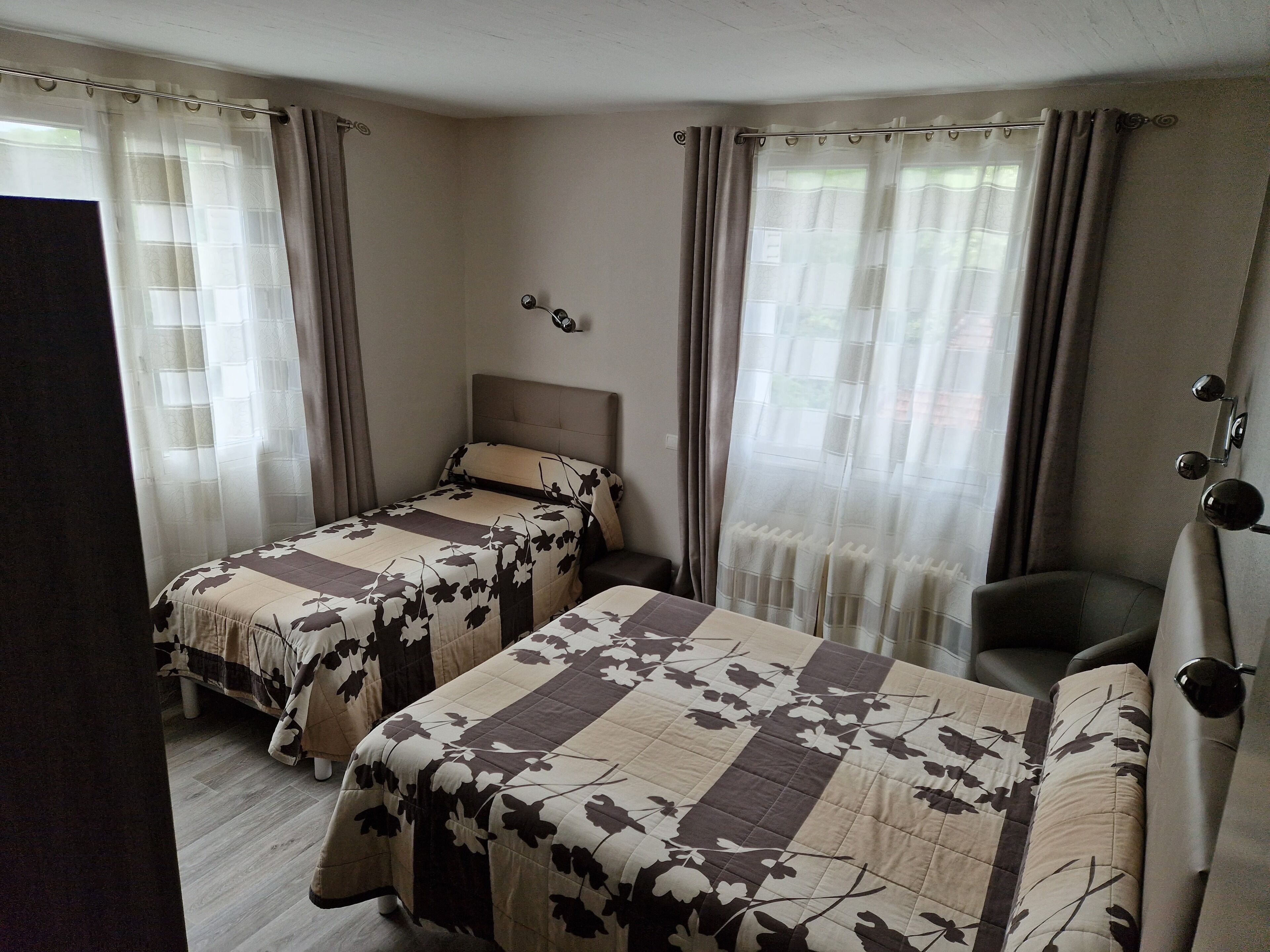Habitación de hotel con dos camas, cabecera, una silla y cortinas.