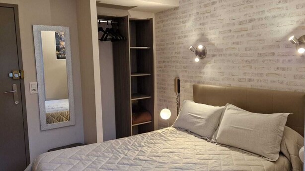 A bedroom with a bed, a wardrobe, a mirror, and a wall with a brick pattern. - Le Faubourg (Figeac)